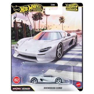 White Koenigsegg CC850 Hot Wheels die-cast car on retail blister pack with a beach sunset backdrop and palm trees in the background.